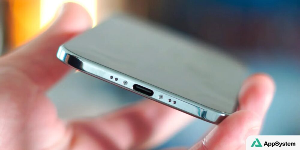 Gros plan d’un iPhone tenu entre les doigts, port USB-C visible.