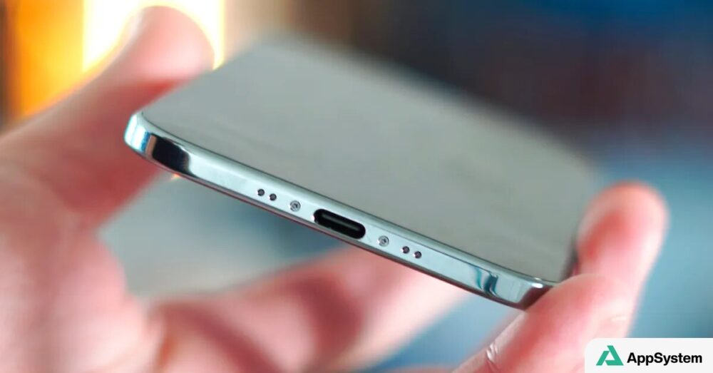 iPhone tenu en main, montrant son port USB-C et ses haut-parleurs.