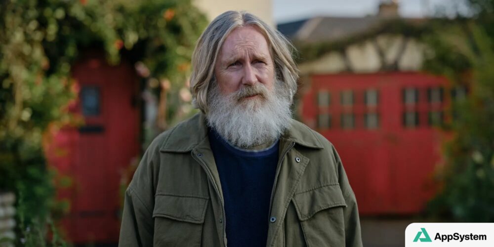 Portrait rapproché d’un homme barbu devant une maison rouge