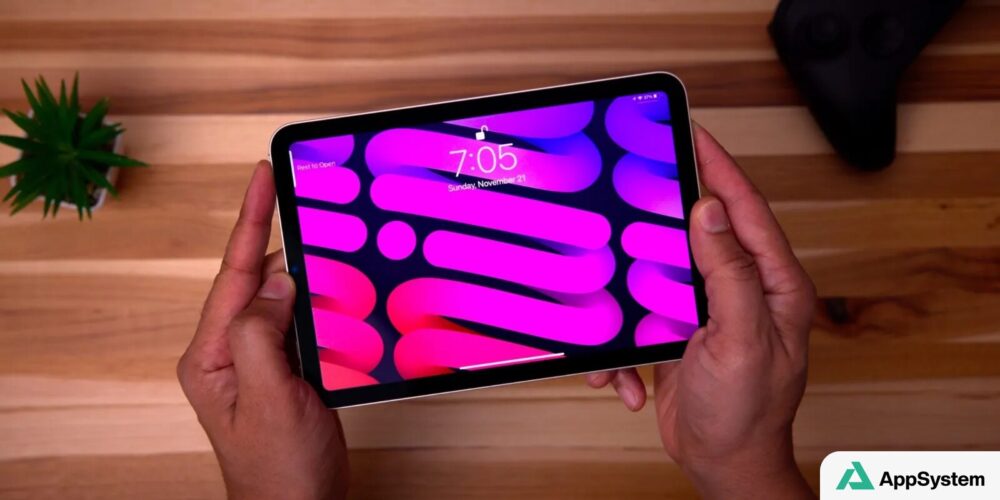 iPad mini tenu par deux mains, écran coloré affichant l’écran verrouillé