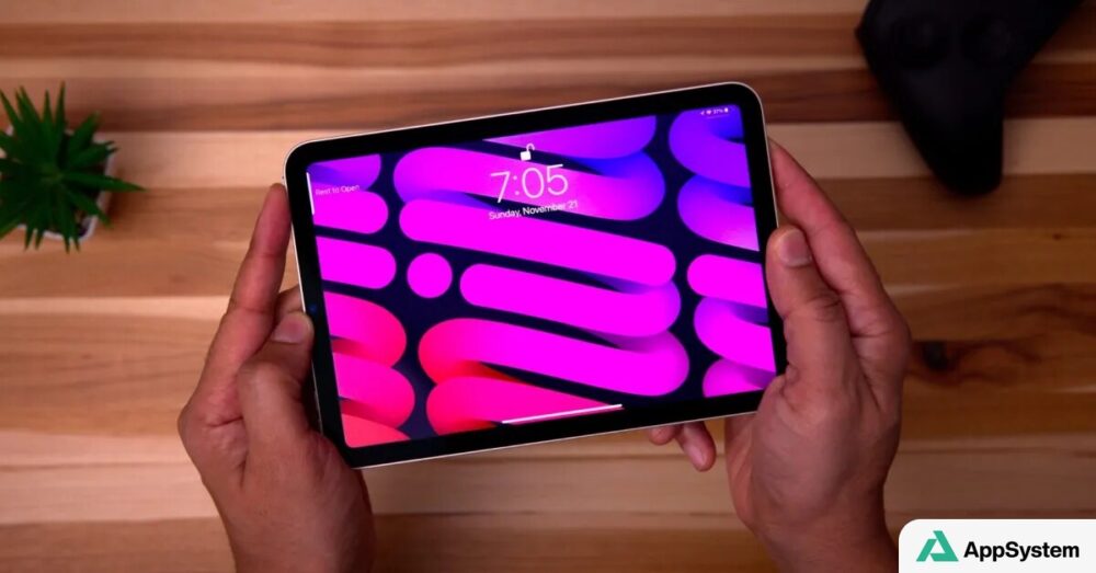 iPad mini tenu à la main, écran allumé sur une table en bois