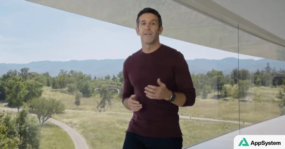 John Ternus s’exprime dans un bâtiment Apple vitré, devant un paysage arboré.
