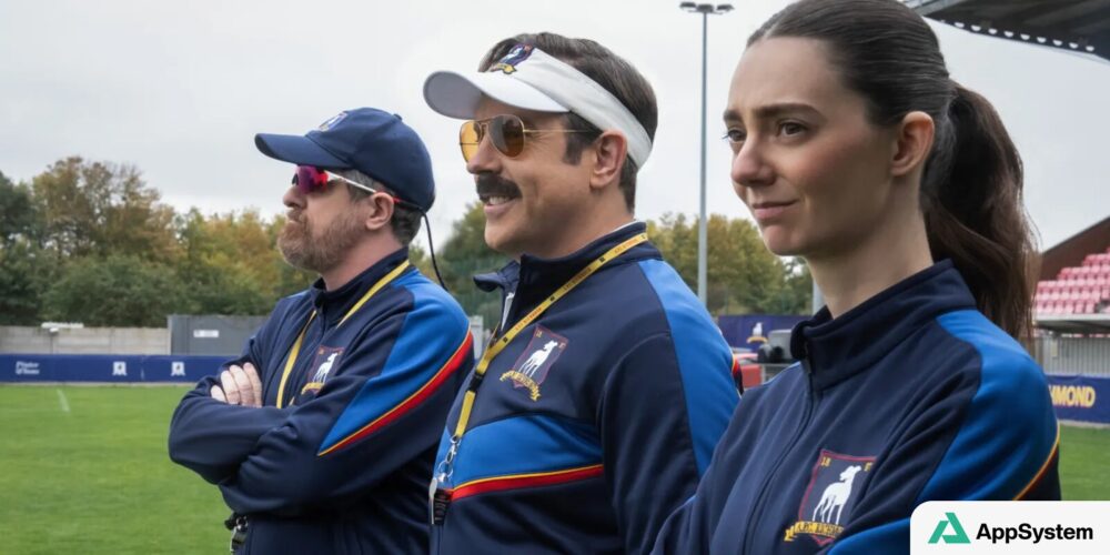 Jason Sudeikis et deux entraîneurs posent sur un terrain de football